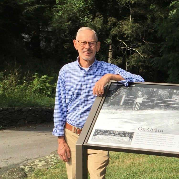 Roger Kolp, a white man wearing a plaid button up, stands next to a sign at Hyde Park