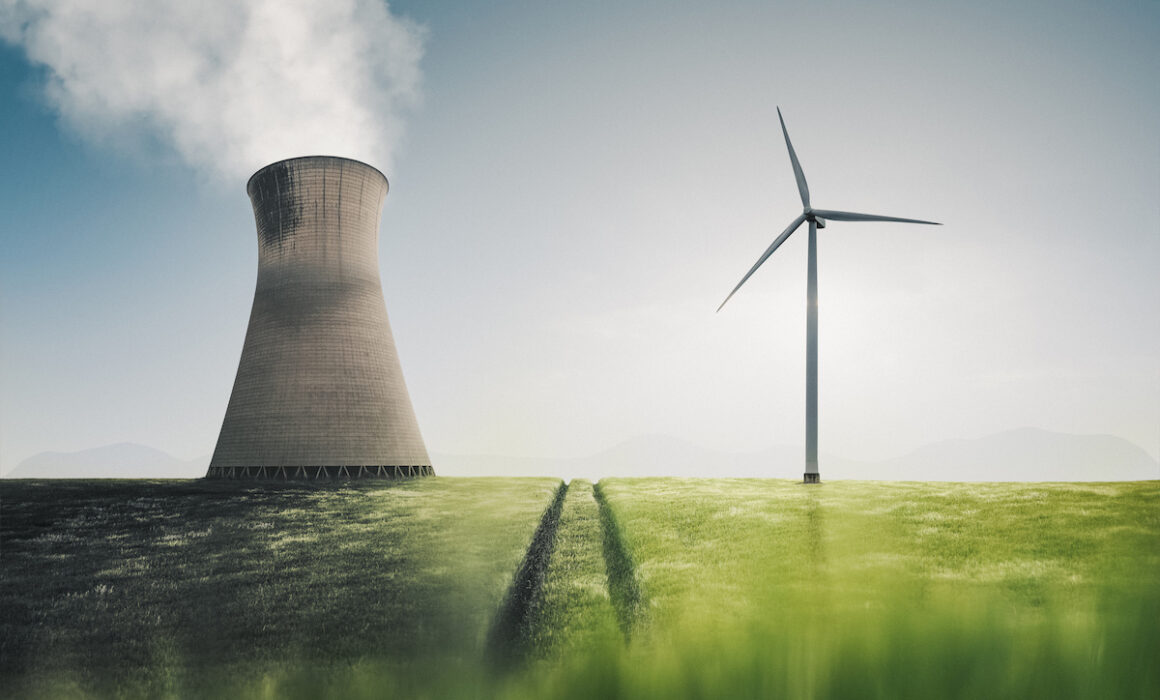 Low angle shot showing a power station and a wind turbine side by side in an agricultural field