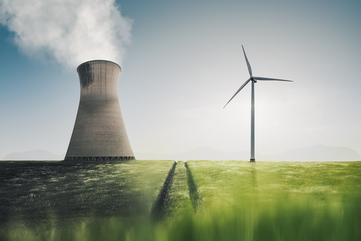 Low angle shot showing a power station and a wind turbine side by side in an agricultural field