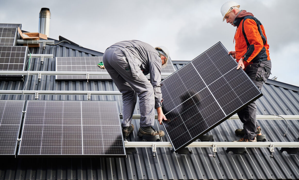 Technicians carrying photovoltaic solar module while installing solar panel system on roof of house