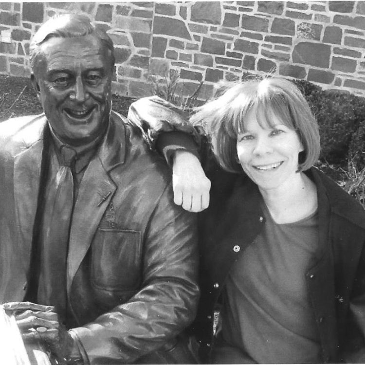 Laurie Squire, a white woman poses with the a statue at the FDR Presidential Library.